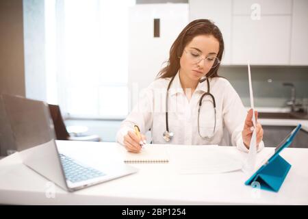 telemedicine. A woman doctor is working from home because of the Cowid-19 coronavirus pandemic. She consults patients online. Stock Photo