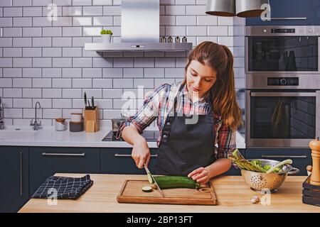 Young woman cutting zuchini on wooden board in her modern kithcen Stock Photo