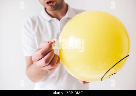 Young man isolated over white background. Cut view and close up of guy holding needle in hand and ready tp piecrce up yellow balloon Stock Photo