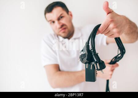 Young man isolated over white background. Electrician guy with cords hold them in hands in front camera. Blurred and defocused picture Stock Photo