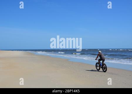 A man rides a bike along the shoreline in Nags Head on the Outer Banks of North Carolina. Stock Photo