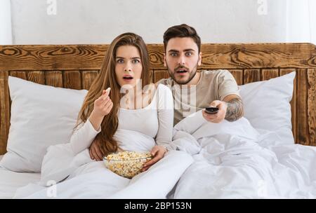 Movie in bed concept. Surprised husband and wife watching tv Stock