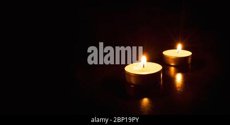 Two burning candles on a black background. Stock Photo