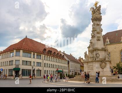 Tourists standing before the 18th century Holy Trinity Statue on Szentharomsag ter in the Buda Castle District with the Burg Hotel in the background Stock Photo