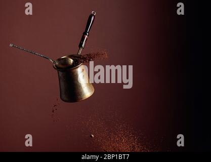 Old copper coffee maker and a spoon with ground coffee in motion. Spilled coffee ground and beans in motion. Brown background. Stock Photo