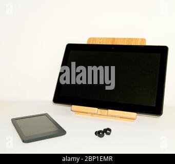 Still life with an e-book and a tablet on a wooden lift stand together with some wireless headphones on a white background Stock Photo