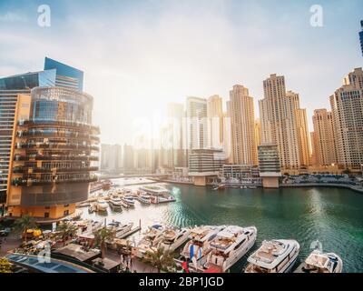 Dubai Marina promenade and canal with luxury yachts, boats and skyscrapers in morning sunlight, United Arab Emirates.