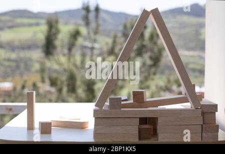 Building from wooden cubes and rods. A photo was taken on the table. Forest mountain landscape in the background. Close up. Stock Photo