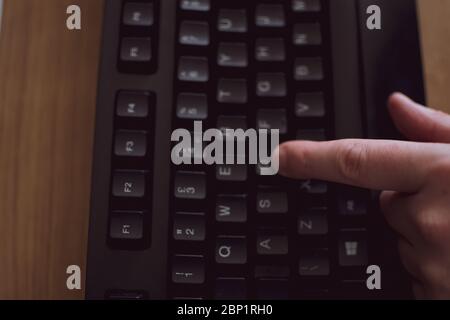 One hand visible as a person types on the letter D on a black keyboard Stock Photo