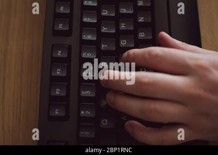 Top down of a hand typing on a black key board on a wooden desk Stock Photo