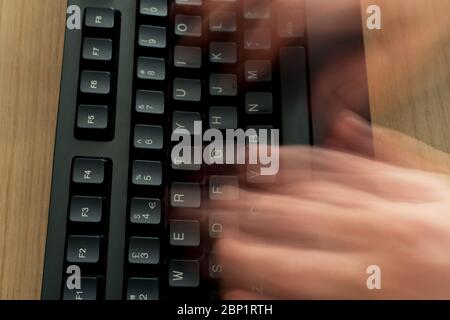 Blurred hands due to fast typing on a black keyboard on a wooden desk in a home office Stock Photo