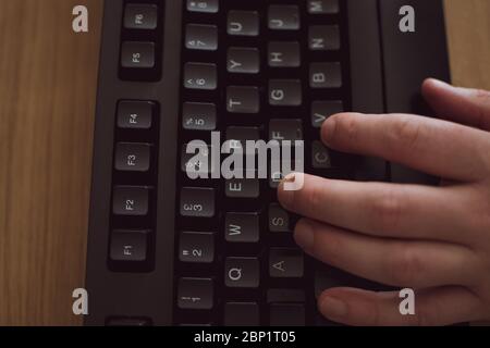 Top down of a hand typing on a black key board on a wooden desk Stock Photo