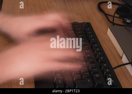 Blurred hands due to fast typing on a black keyboard on a wooden desk in a home office Stock Photo