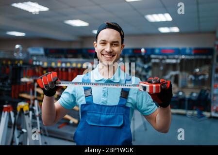 Smiling worker holds measuring tape in tool store Stock Photo