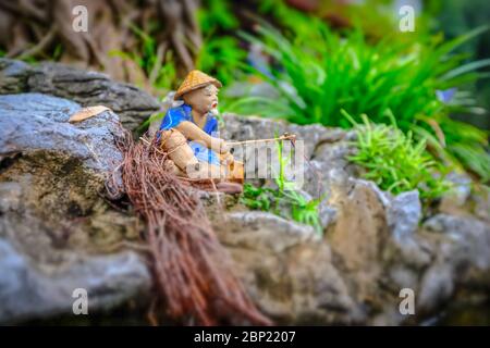 Small figurine representing a fisherman in natural setting with blurred green and rocky background, Hanoi, Vietnam Stock Photo