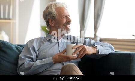 Happy elderly man resting on sofa with cup of tea. Stock Photo