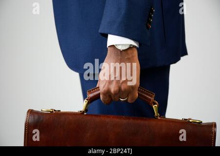 Close up of stylish young dark skinned businessman in formal wear holding briefcase. Business suit. Side view, mid section. Stock Photo