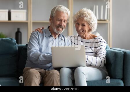 Happy older spouses sitting on sofa, looking at computer screen. Stock Photo