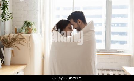 Loving couple wrapped in cover having romantic moment at home Stock Photo