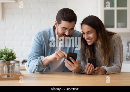 Happy couple have fun at home using cellphones in kitchen Stock Photo
