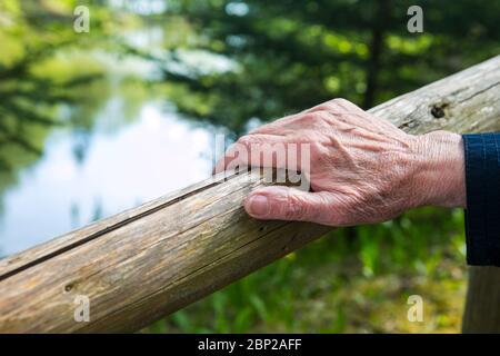 close-up of old womans hand resting at a railing in nature Stock Photo