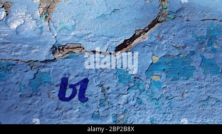Cracked painted surface of old cement wall covered with many layers of blue flaking paint and cutout blue Cyrillic letter Y closeup Stock Photo