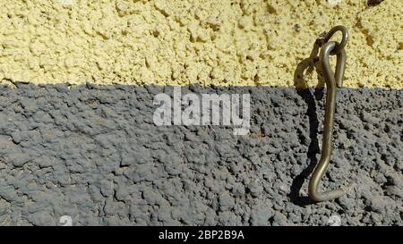 Rusty metal hook of obsolete latch hanging on rough wall background of yellow and grey stripes. Texture of uneven plaster wall and old hasp Stock Photo