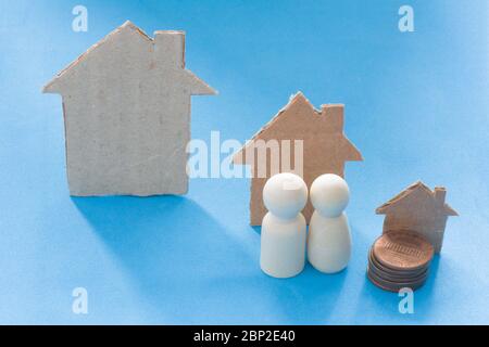 Young couple on cardboard houses different size and stack of coins background. Larger home purchases, moving house and real estate. Concept of sale or Stock Photo