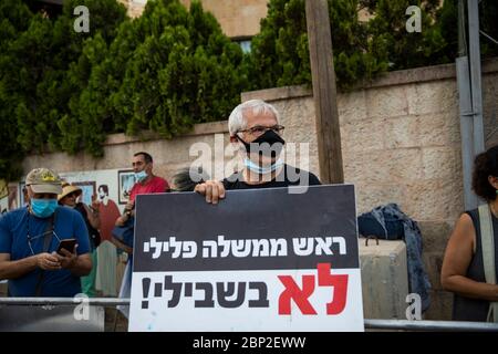 Jerusalem, Israel. 17th May, 2020. A protester wearing a face mask holds a placard during a demonstration against the forming of the new Israeli government, led by leader of the Likud party Benjamin Netanyahu and leader of the Blue and White party Benny Gantz, outside Israeli Prime Minister Netanyahu's Residency. Netanyahu has been sworn in as Israel's new prime minister, at the head of a unity government with former rival Benny Gantz, ending a nearly 18-month political crisis. Credit: Ilia Yefimovich/dpa/Alamy Live News Stock Photo
