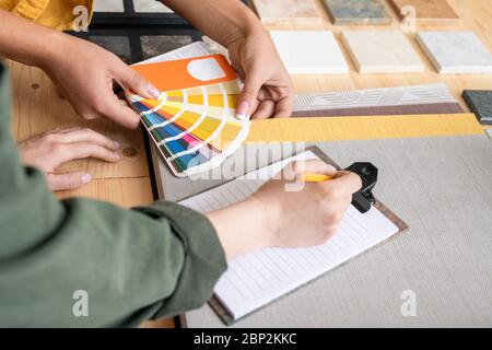 Hands of female designer holding palette over table while showing colors to colleague during work over new order or project at meeting Stock Photo