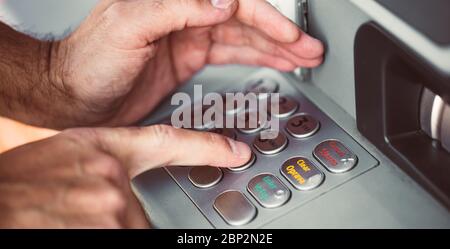 Man entering a PIN code for his credit card at an ATM, withdrawing money, finance concept Stock Photo