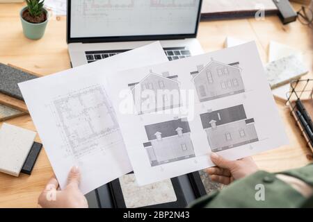 Hands of female architect holding papers with sketch of new house and its plan over table with laptop and samples of marble tile Stock Photo