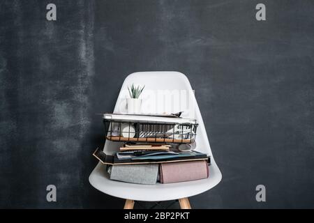 Basket with office supplies, folded textile samples, business documents, laptop and flowerpot with small green plant on white chair Stock Photo