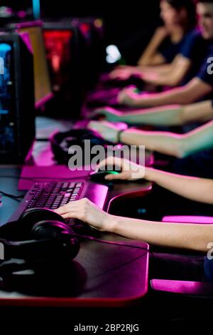 Row of hands of young contemporary e-sport clubbers sitting by desks in front of computer monitors and playing cyber games Stock Photo