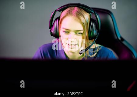 Young female operator in headset looking at computer screen while consulting clients or gamer playing e-sport video game in club Stock Photo