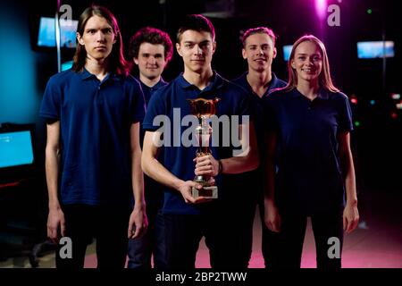 Team of five young champions in cybersports and network gaming competition standing in row in contemporary e-sports club Stock Photo