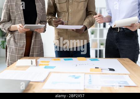 Mid section of three colleagues standing in row by desk with papers while brainstorming or preparing for presentation before conference Stock Photo