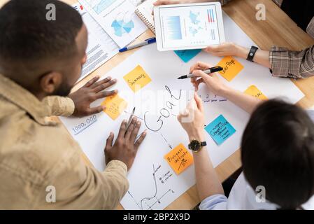 Hands of intercultural analysts or brokers discussing financial data and making goals table with new ideas written on notepapers Stock Photo