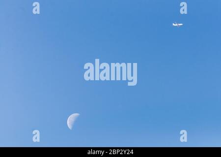 airplane illuminated by sunlight flying over a waning moon in the morning illuminated sky. freedom concept. travel, desire to fly Stock Photo