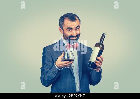 A mature happy man holding showing offering a glass of red wine looking at you camera smiling happily. Mixed race bearded model isolated green backgro Stock Photo
