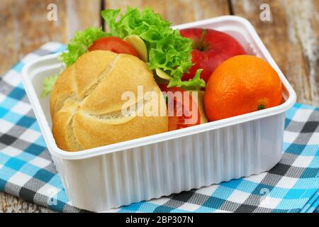 Healthy school lunchbox containing roll with cheese, lettuce and tomato, red apple and mandarine Stock Photo