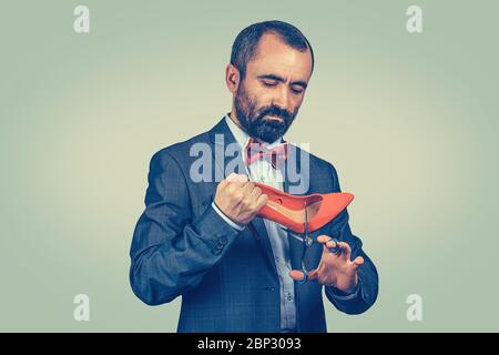 Closeup portrait middle aged man holding shoe and scissors about to cut them in studio. Mixed race bearded model isolated on green yellow gradient bac Stock Photo