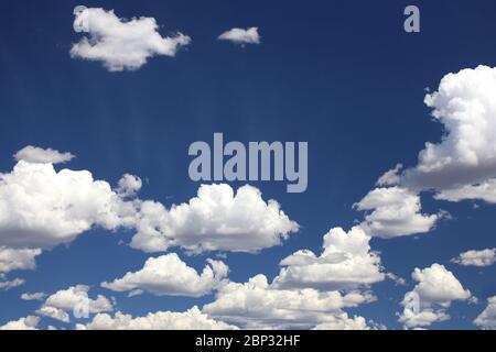 Puffy cumulus clouds set against a deep blue sky with subtle sun rays Stock Photo