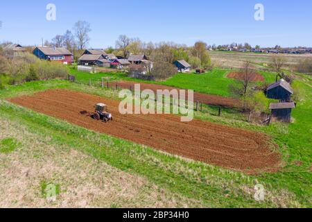 Tractor plows a small field in the village before planting vegetables. Aerial rural landscape on the horizon height view Stock Photo