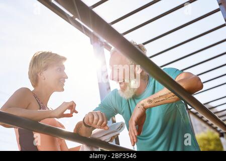 Taking a break. Happy sporty mature couple standing near parallel bars and discussing something. Resting after morning workout outdoors Stock Photo