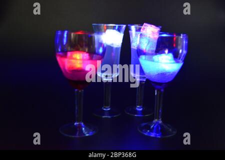 Four glasses with bright different colors of luminous led ice cubes are located on a black background. Stock Photo