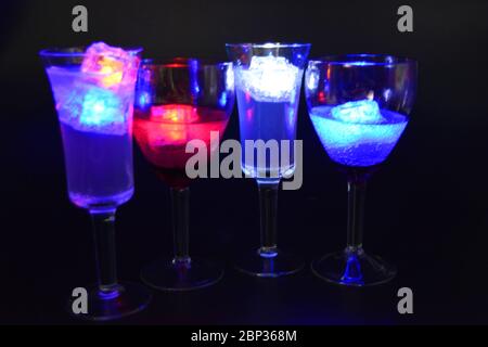 Four glasses with bright different colors of luminous led ice cubes are located on a black background. Stock Photo