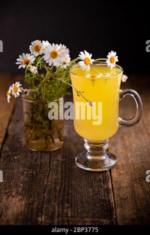 Chamomile tea in a glass cup on a wooden table. Bouquet of medicinal chamomile. Aromatherapy and herbal medicine. Daisies are field. White flowers. Stock Photo