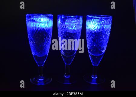 Crystal champagne glasses with carvings in the form of snowflakes are located on a black matte background. Bright multicolor doidic glowing ice cubes Stock Photo