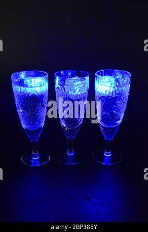 Crystal champagne glasses with carvings in the form of snowflakes are located on a black matte background. Bright multicolor doidic glowing ice cubes Stock Photo